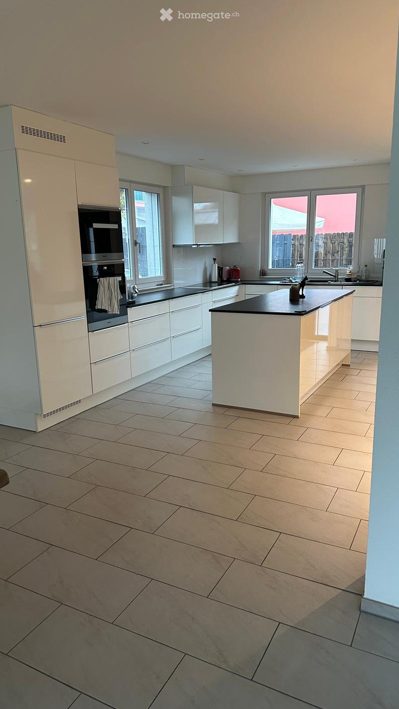 Modern kitchen with white cabinets, a central island, and tiled flooring. Features include a built-in oven, refrigerator, and sink with a window above.