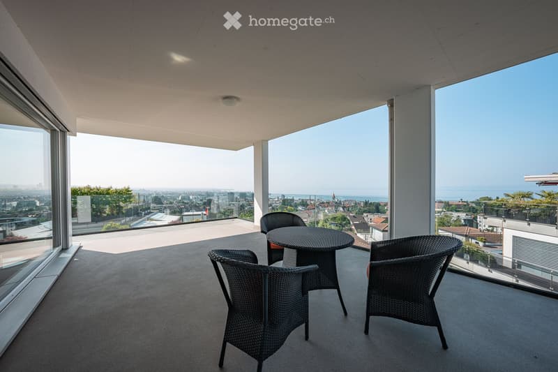 Modern balcony with panoramic city and sea views, featuring a round table and four wicker chairs.