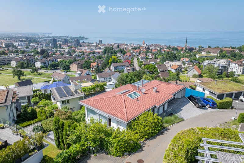 Aerial view of a suburban neighborhood with multiple houses, solar panels, and a scenic view of a lake and city skyline in the background.