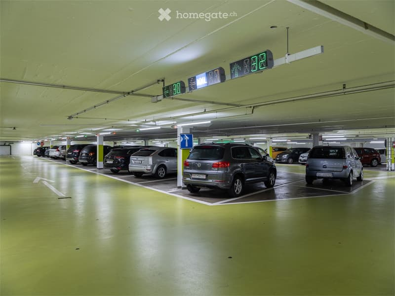 Underground parking lot with multiple parked cars, marked parking spaces, and directional signage.