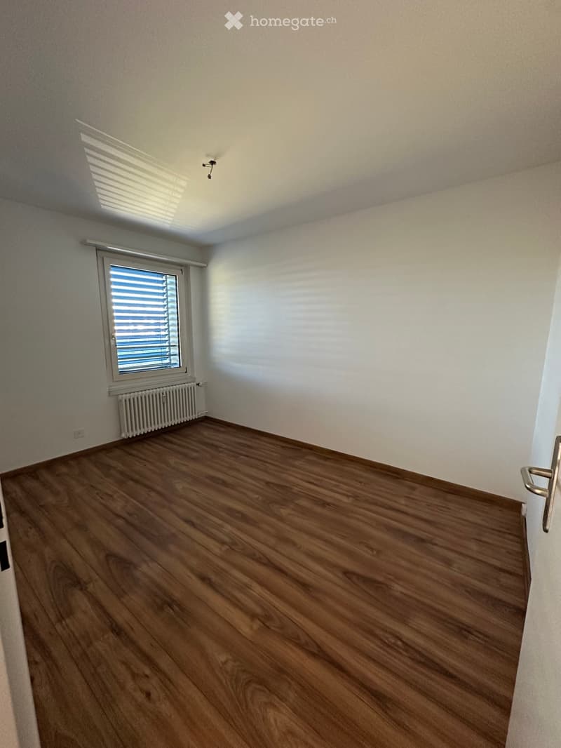 Empty room with wooden flooring, white walls, and a window with blinds. A radiator is visible below the window.
