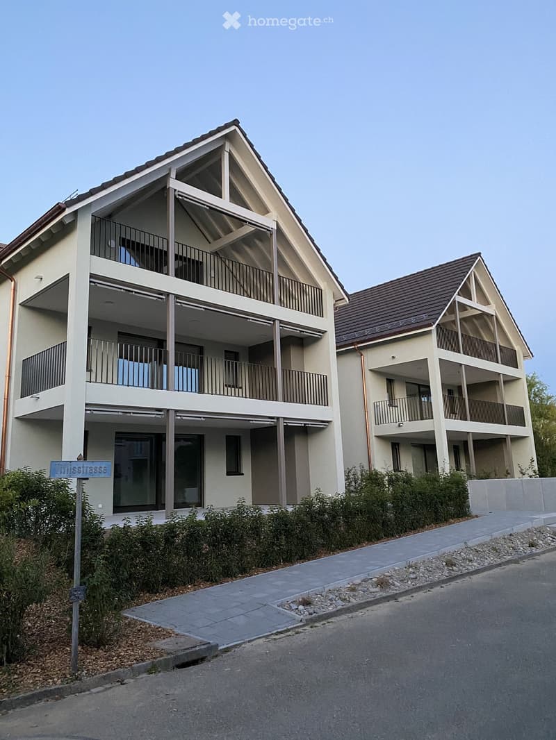 Two-story residential building with balconies, modern design, and a sloped roof.