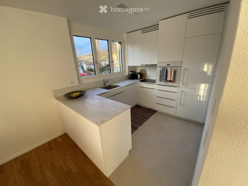 Modern kitchen with white cabinets, marble countertop, sink, oven, coffee maker, and a bowl of fruit on the counter.