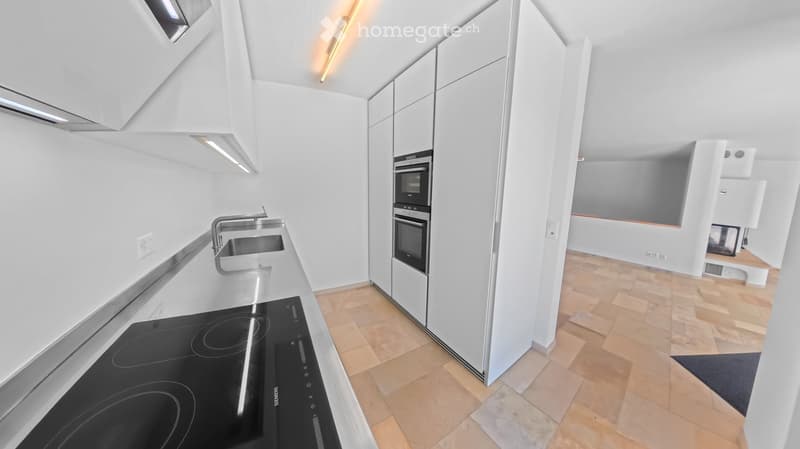 Modern kitchen with white cabinets, stainless steel sink, induction cooktop, and built-in ovens. Light wooden flooring and sleek design.