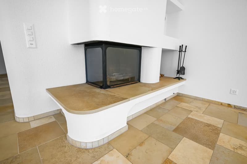 Modern fireplace with a sleek black frame and glass front, placed on a tiled platform with beige tiles and a white curved base.