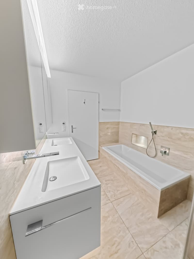 Modern bathroom with a double sink vanity, bathtub, and sleek fixtures.