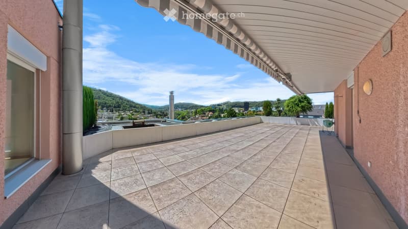 Spacious balcony with tiled flooring, covered awning, and scenic view of the valley and surrounding greenery.