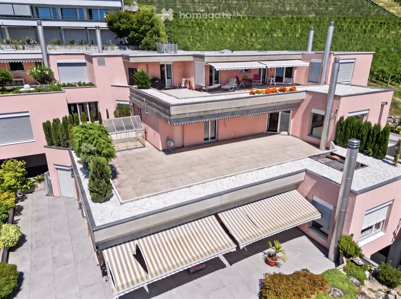 A modern, two-story pink building with multiple terraces, outdoor seating, and surrounding greenery.