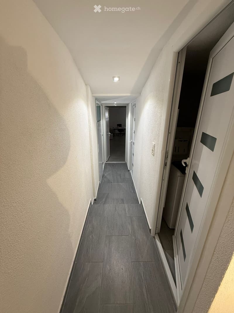 empty corridor with a tiled floor, white walls, two doors on each side, one with a washing machine inside