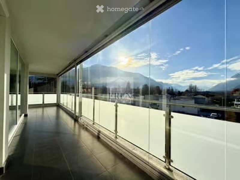 Spacious balcony with large glass windows and a modern glass railing, offering a scenic mountain view.