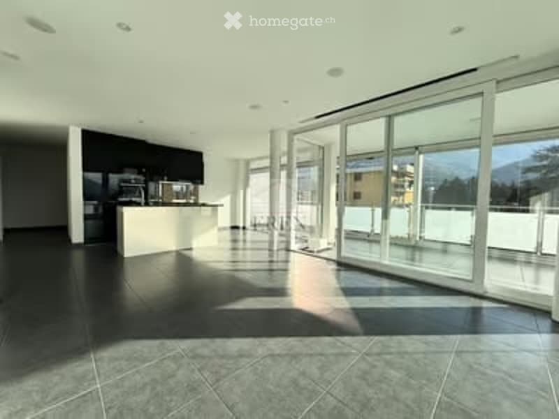 Modern, minimalist kitchen with dark tiled floor, white cabinetry, built-in appliances, and large glass sliding doors leading to a balcony.