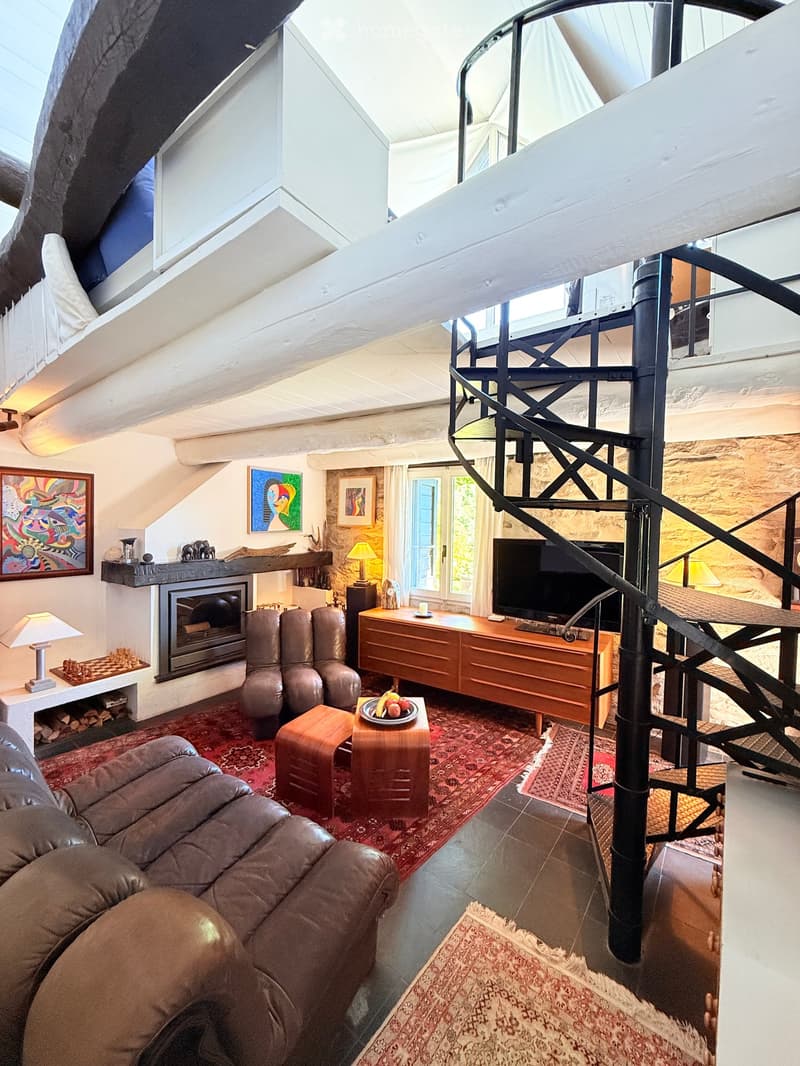 Cozy living room with exposed wooden beams, fireplace, leather sofa, armchairs, coffee table, TV, and artwork on the walls.