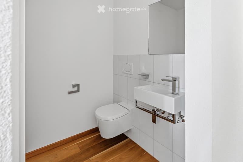 Modern bathroom with white tiled walls, wooden flooring, a toilet, a sink with a modern faucet, and a mirror above the sink.