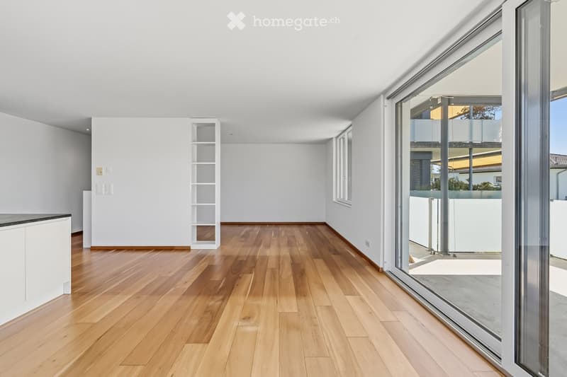 Empty room with light wooden flooring, white walls, and large glass sliding doors leading to an outdoor area.