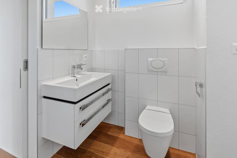 Modern bathroom with white tiles, a white sink with a cabinet, a toilet, and a large mirror above the sink.