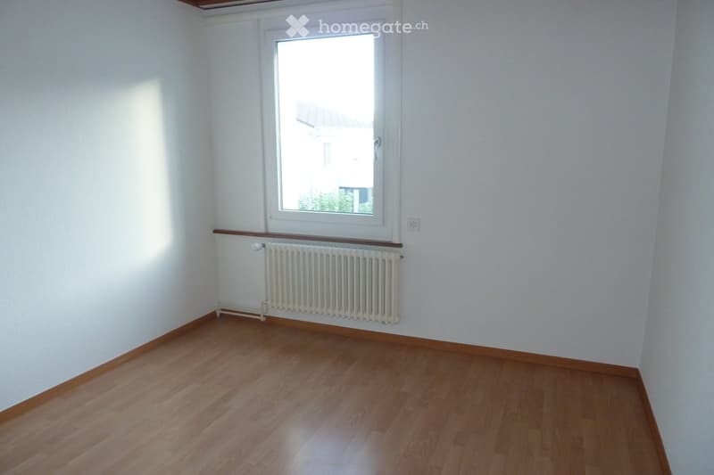 Empty room with wooden flooring, white walls, a window, and a radiator below the window.