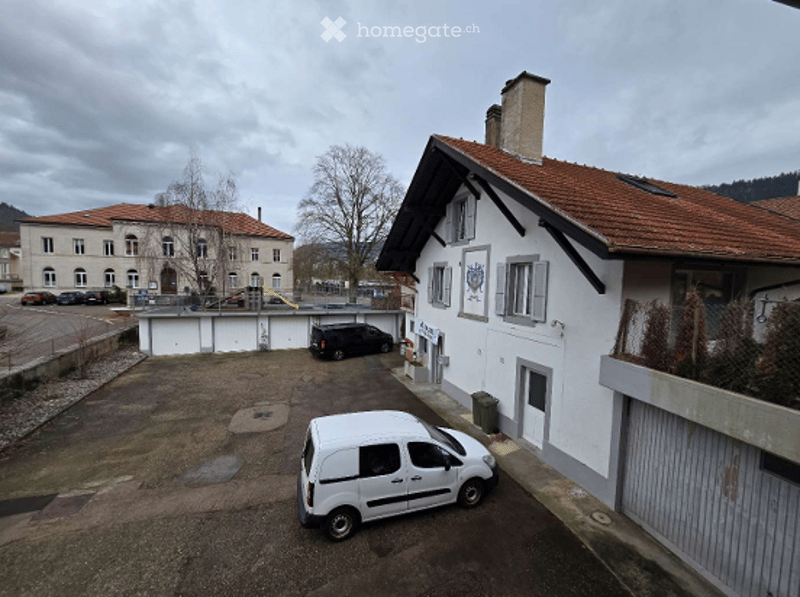 white house with brown roof, garage, parking lot, van parked, another building in the background