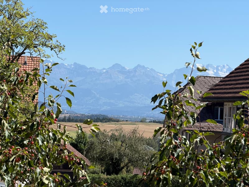 Scenic outdoor view with mountains in the background, houses, trees, and a clear blue sky.