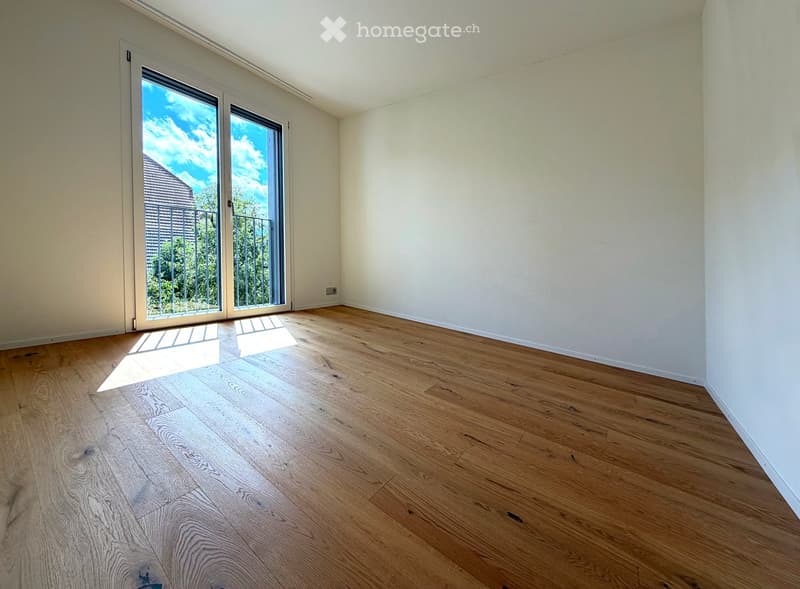 Empty room with light wooden flooring and white walls, featuring a large sliding glass door leading to a balcony.