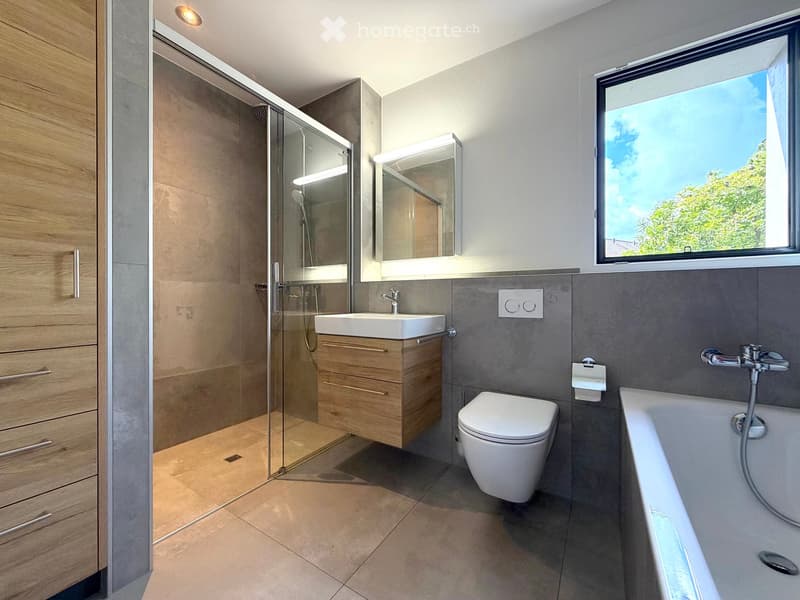 Modern bathroom with a large window, featuring a sink, toilet, bathtub, shower, and wooden cabinet.