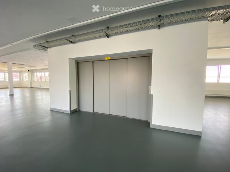 Empty room with white walls, grey floor, and a large white door. No furniture or equipment visible.