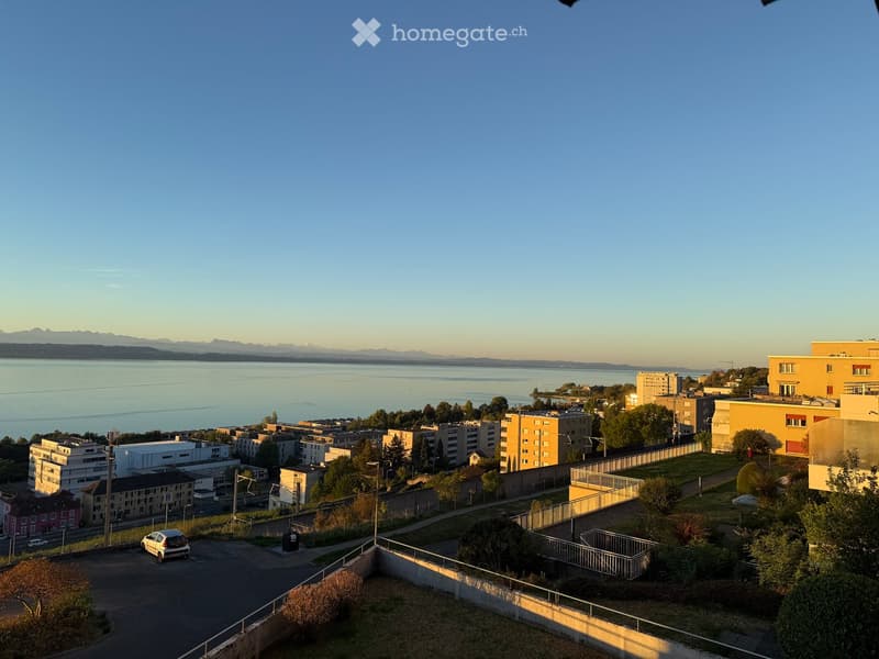 Balcony overlooking a cityscape with buildings, a body of water, and distant mountains.