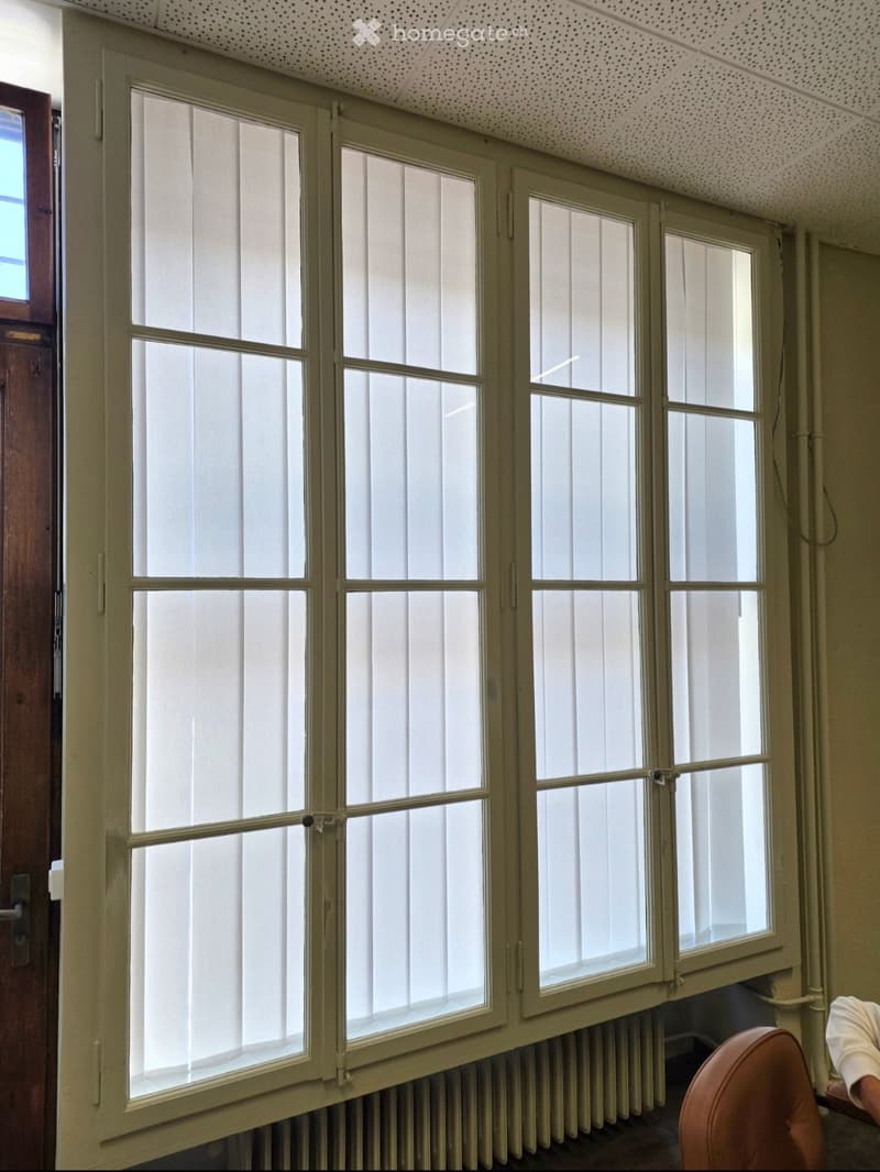 Empty room with large windows, radiator, and a partially visible chair in the corner.