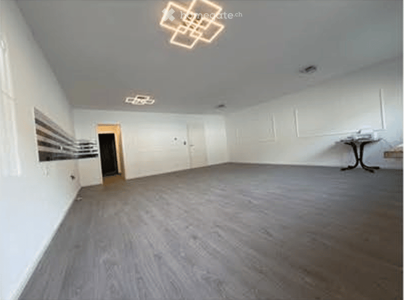 Empty room with white walls, wooden flooring, and a single door leading to another space. The room is completely unfurnished with no visible furniture or equipment.