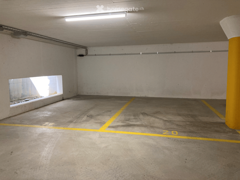 Underground parking space with concrete floors and walls, marked parking spots, and a single window providing natural light.