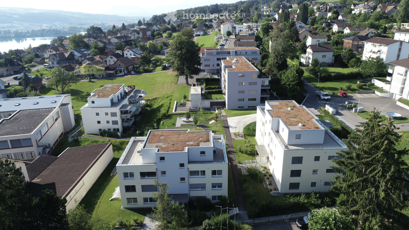 Aerial view of a residential area with multiple apartment buildings, green spaces, parking lots, and a swimming pool.