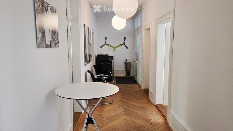 A modern hallway with herringbone wooden flooring, white walls, and contemporary decor including a round white table, chairs, and artwork.