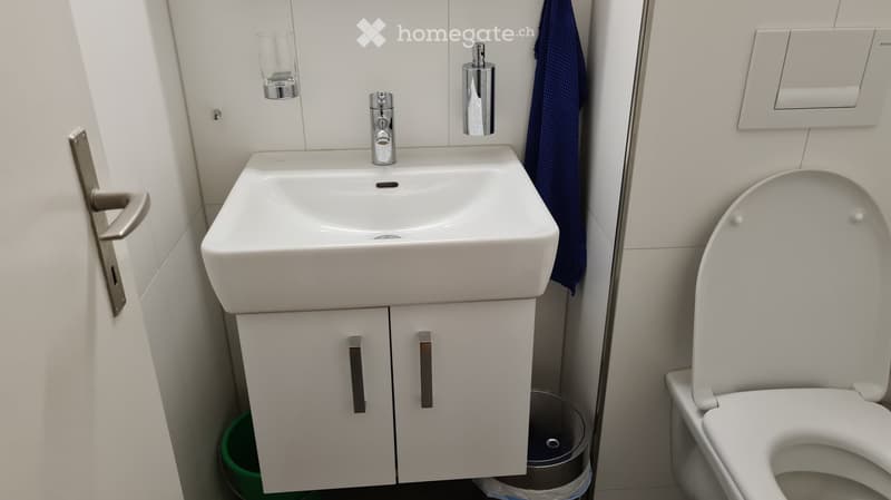 Modern bathroom with a white sink, chrome faucet, mirrored cabinet, toilet, and a blue towel hanging on the wall.