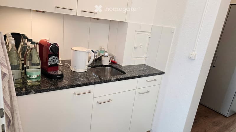 Modern kitchen with white cabinets, granite countertop, coffee maker, kettle, and sink.