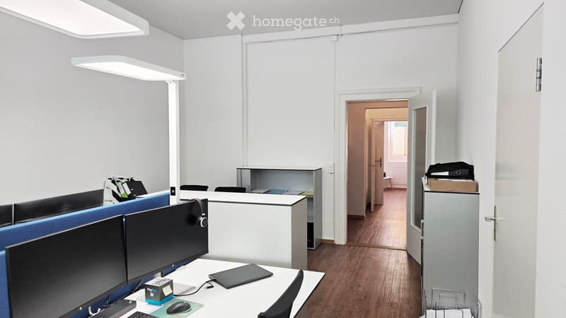 Modern office space with desks, chairs, multiple screens, laptops, and office supplies.