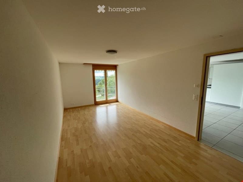 Empty room with wooden flooring, white walls, and a sliding glass door leading to a balcony.