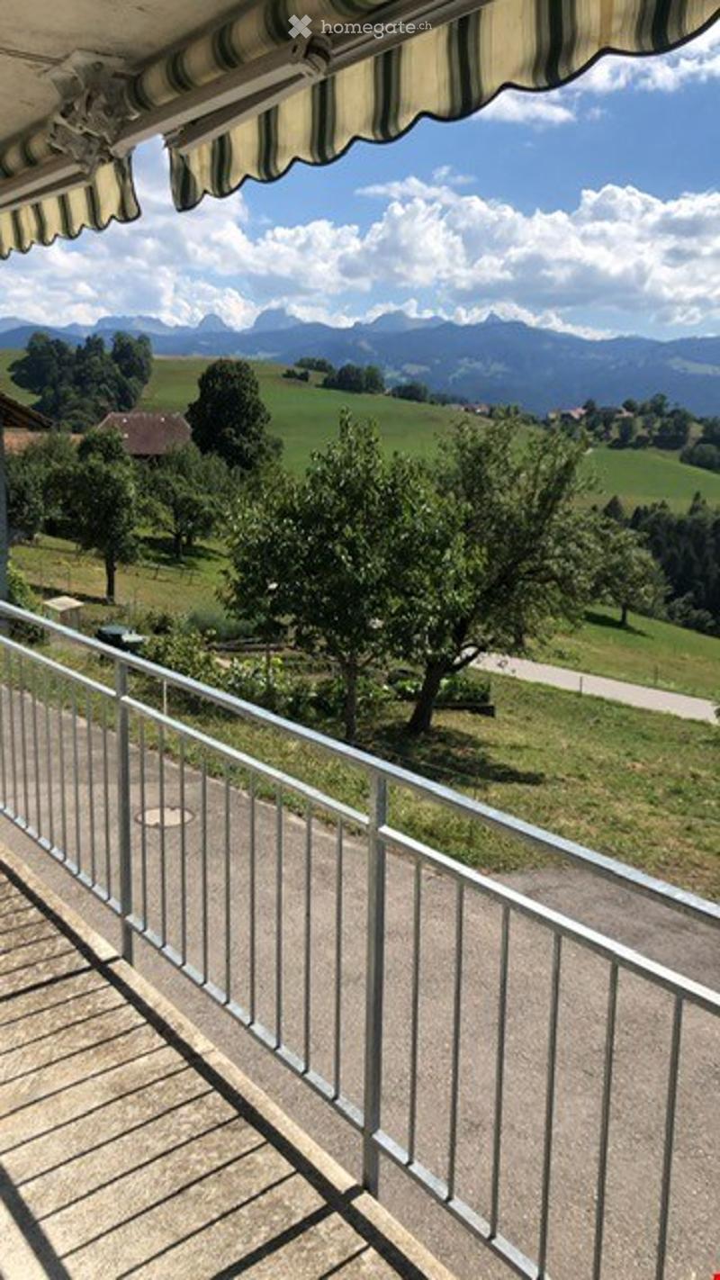 Balcony with metal railing, overlooking a green landscape with trees and mountains in the background.