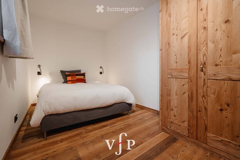 Cozy bedroom with a neatly made bed, wooden wardrobe, and warm lighting.