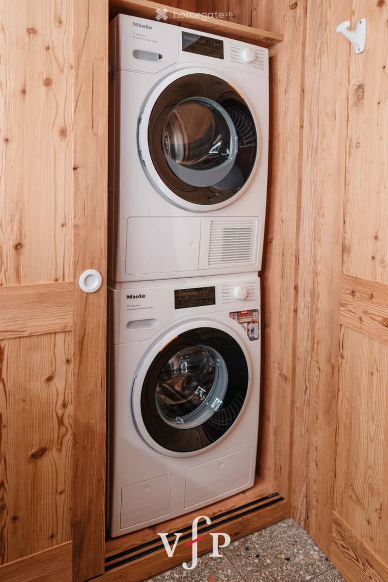 A compact, modern bathroom with a stacked Miele washing machine and dryer unit, wooden panel walls, and a tiled floor.