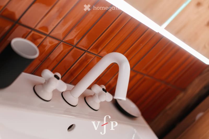 Close-up of a modern white faucet with dual handles mounted on a wooden surface, likely part of a bathroom sink.