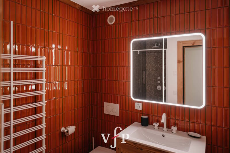 Bathroom with wooden tiled walls, a white sink with a modern faucet, a large illuminated mirror, a towel rack, and a cup on the sink counter.