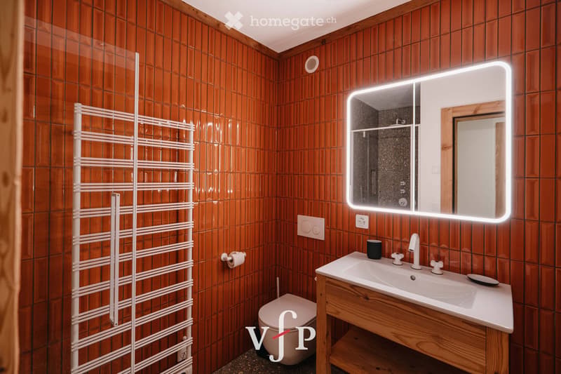 Bathroom with wooden tiled walls, a white towel rack, a sink with a modern faucet, a large illuminated mirror, and a toilet.