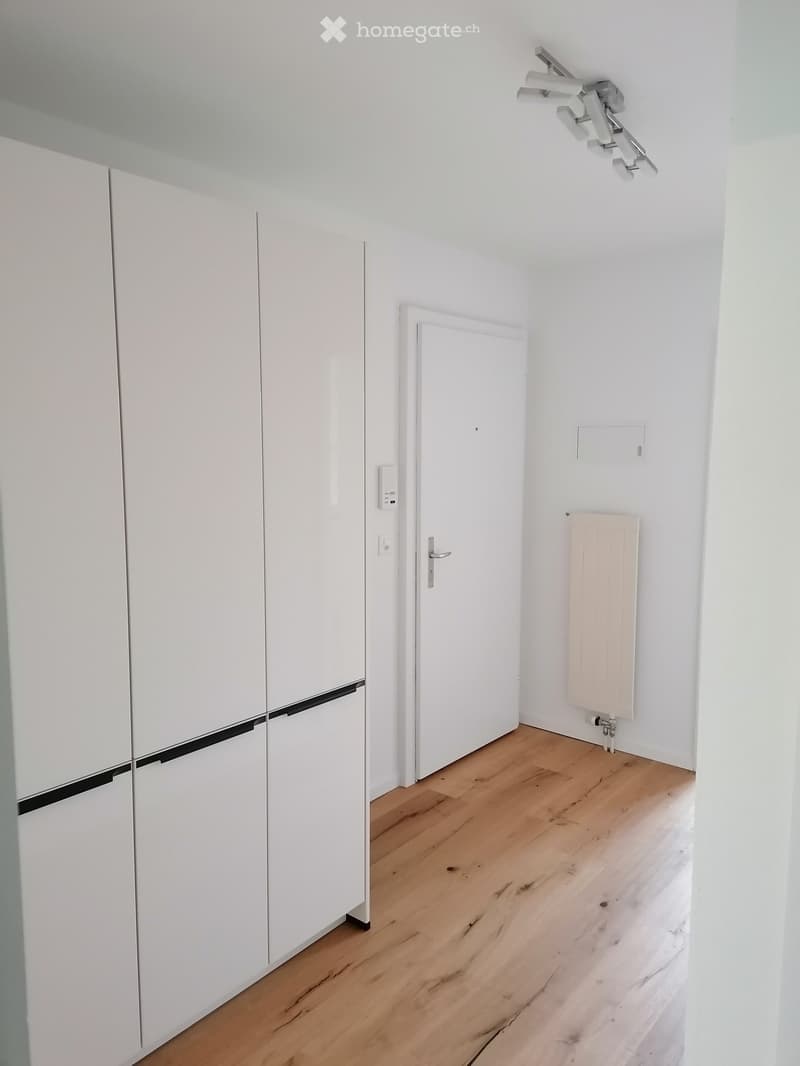Empty room with white walls, wooden floor, white closet, radiator, and a door.