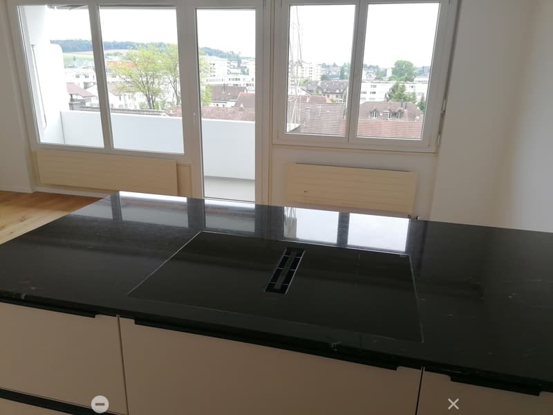 Modern kitchen with black countertop, integrated sink, and large windows offering a view of the cityscape.