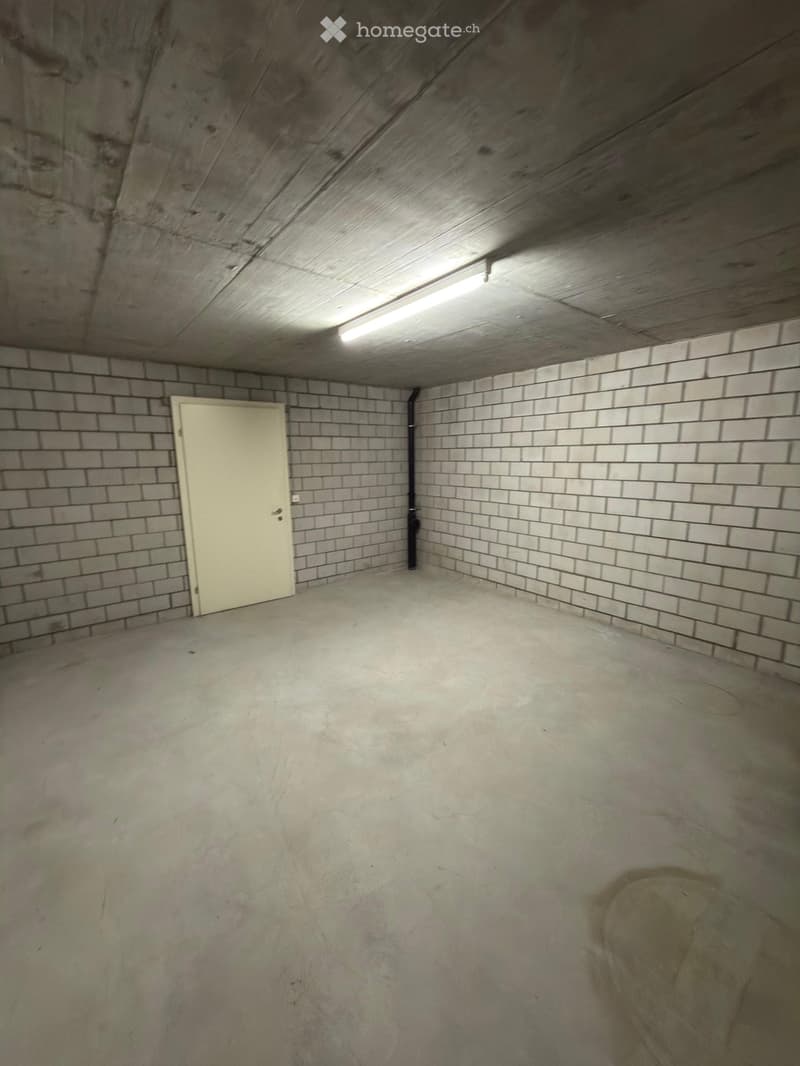 Empty room with concrete floor, brick walls, and a single door. The ceiling has exposed wooden beams and a skylight.
