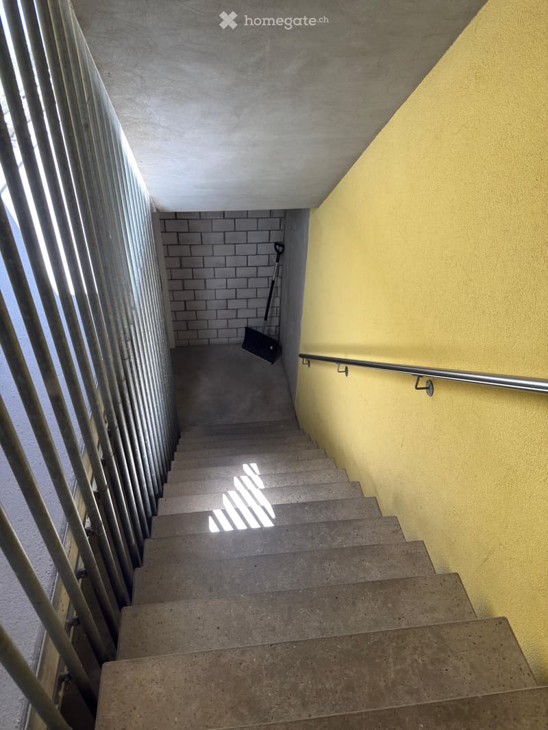 Concrete staircase with yellow walls, metal railing, and a broom leaning against the wall.