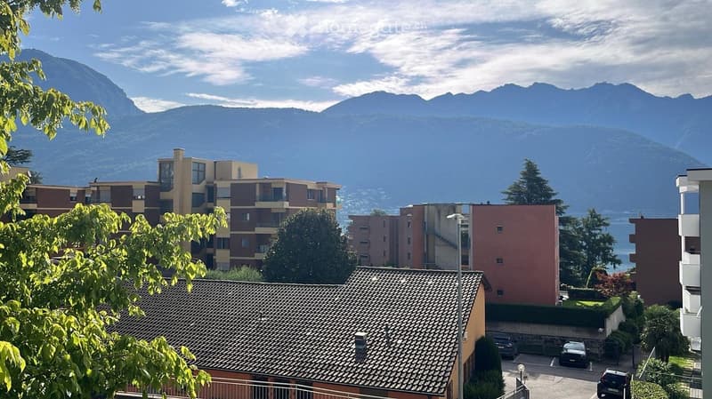 View of a residential area with apartment buildings, parked cars, and a scenic mountain backdrop.