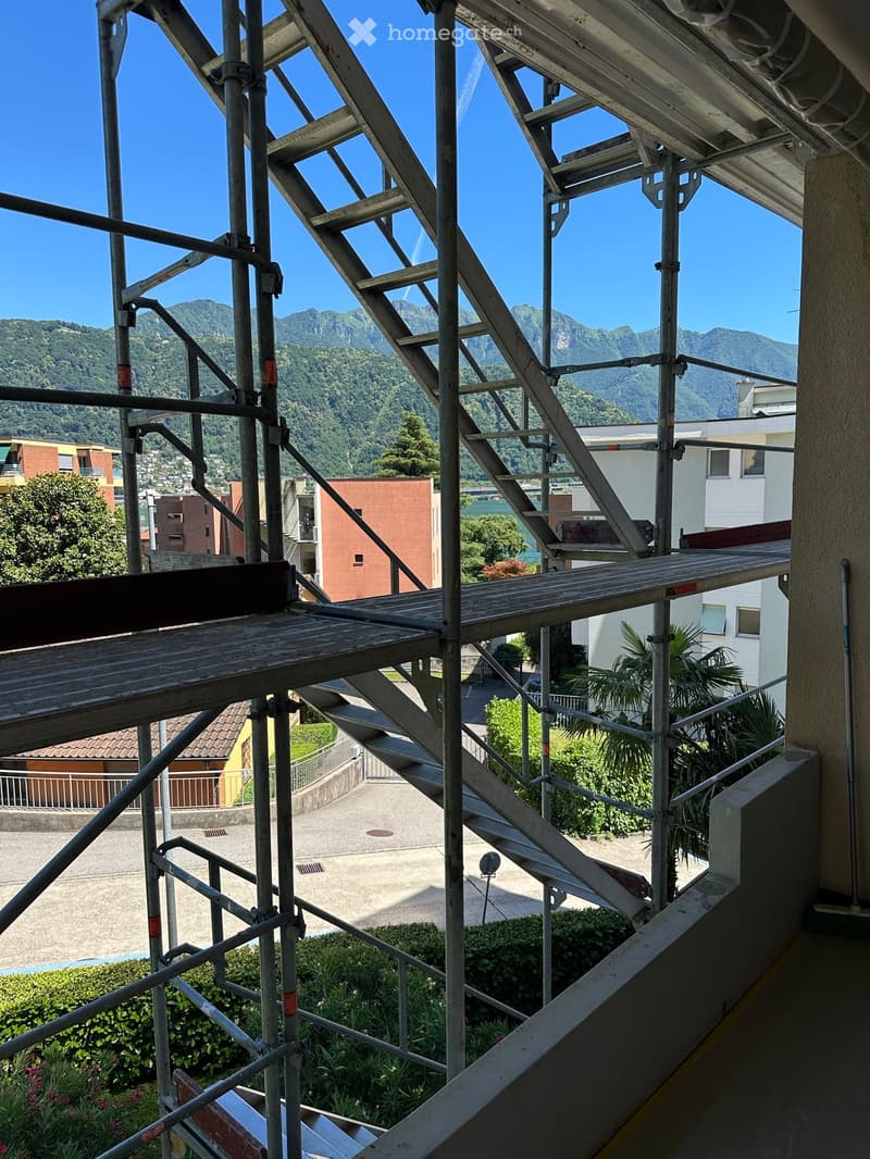 Balcony under construction with metal scaffolding, overlooking a scenic view of mountains and a body of water.