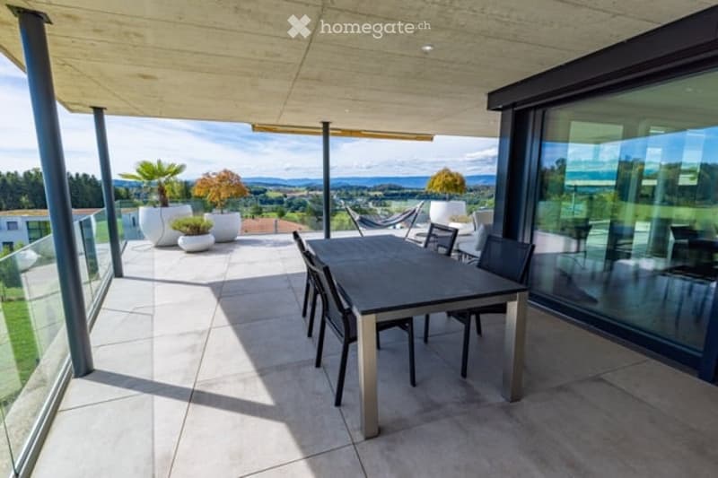 Modern outdoor terrace with a dining table and chairs, large glass windows, and scenic mountain view.