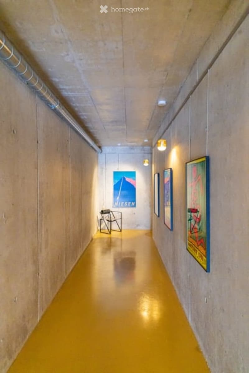 Minimalist hallway with yellow flooring, concrete walls, and framed artwork, illuminated by warm lighting.
