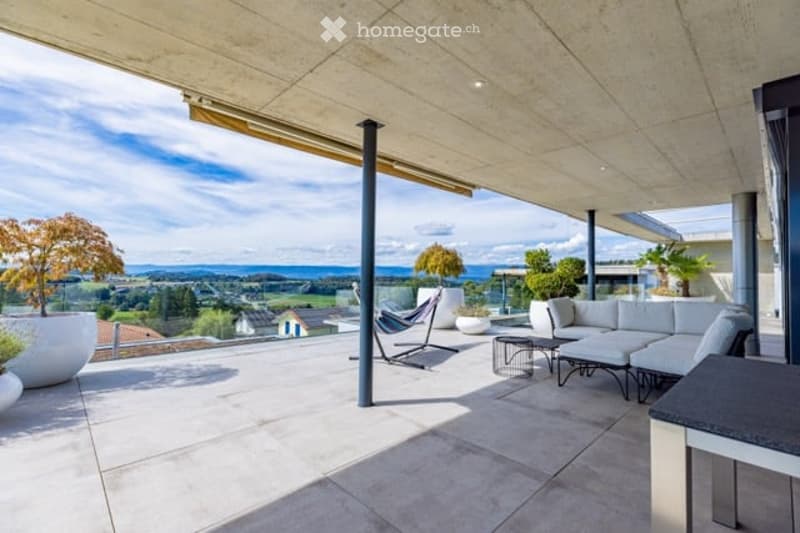 Modern terrace with expansive scenic view, white sectional sofa, glass table, lounge chair, and potted plants.